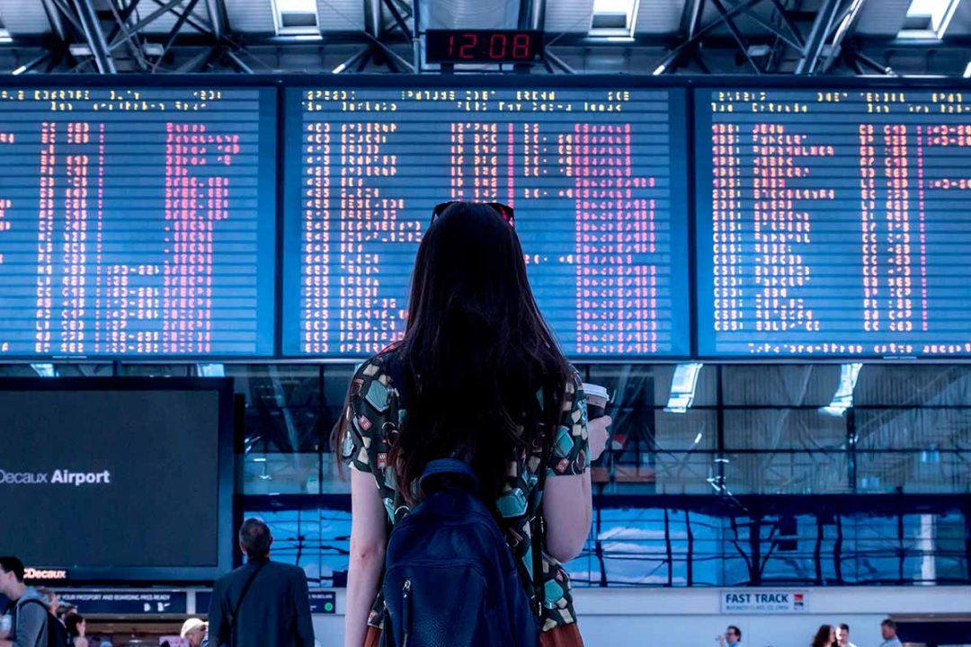Chica antes de viajar mirando panel de vuelos en el aeropuerto
